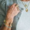 Close-up of a person wearing gold jewelry including rings and a bracelet on a light gray sweater.