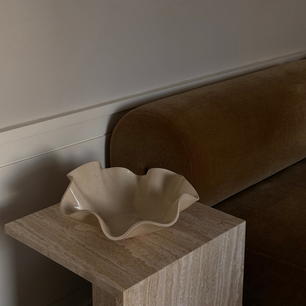 Beige ceramic dish on a wooden surface with a brown sofa in the background