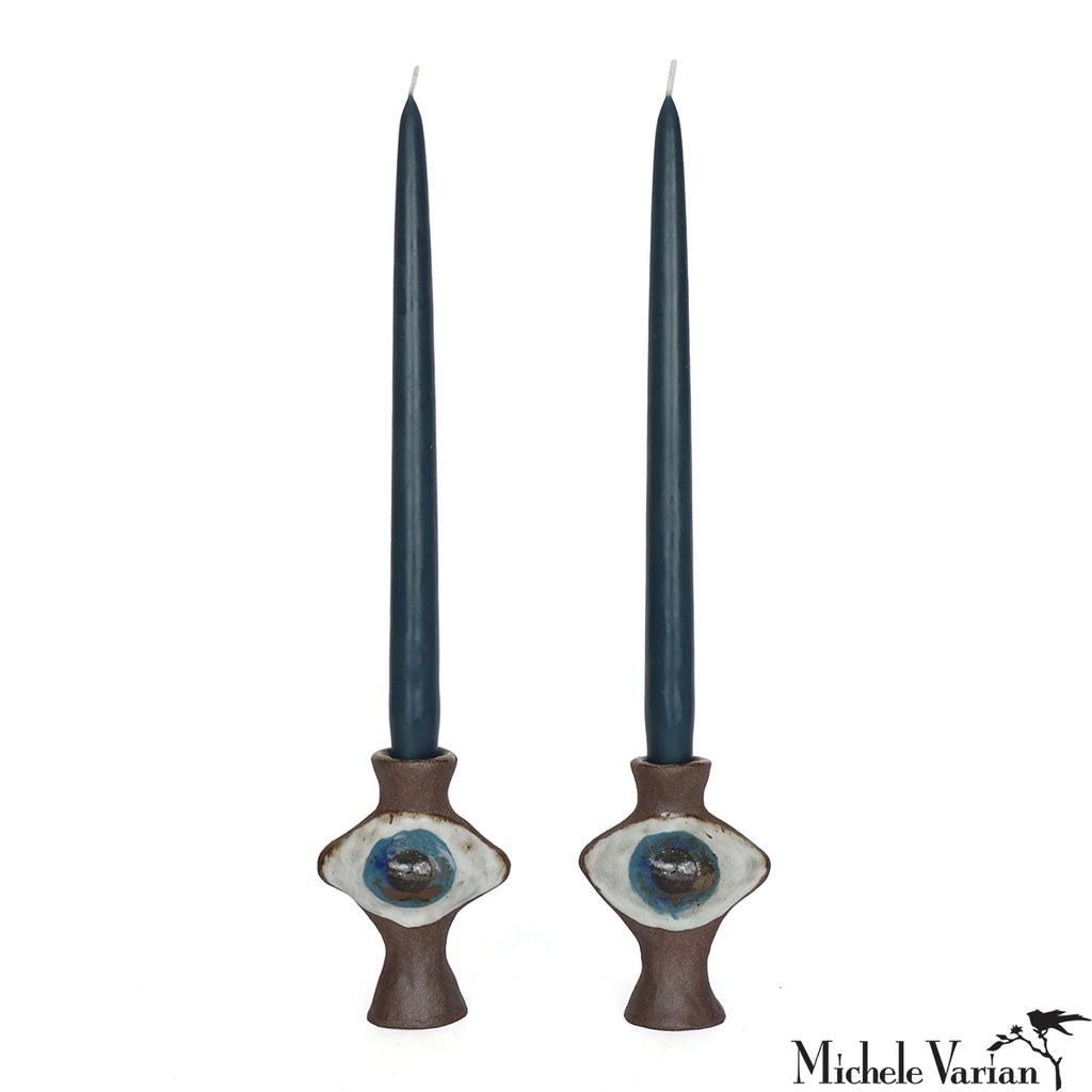 Two dark blue candles in decorative candle holders with a white background