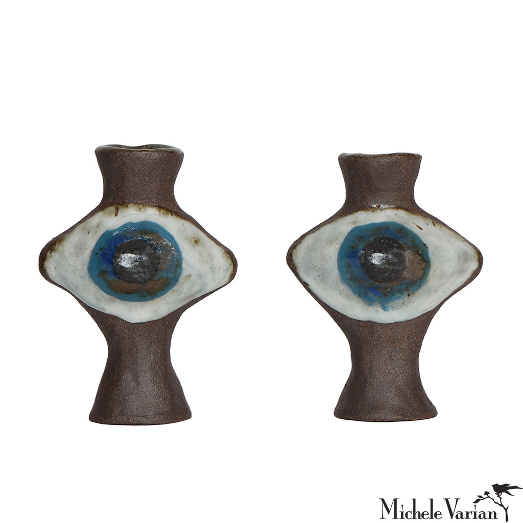 Two ceramic eye-shaped candleholders with brown, white, and blue design on a white background.