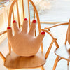 Knitted hand-shaped pillow with red nail polish on a wooden chair