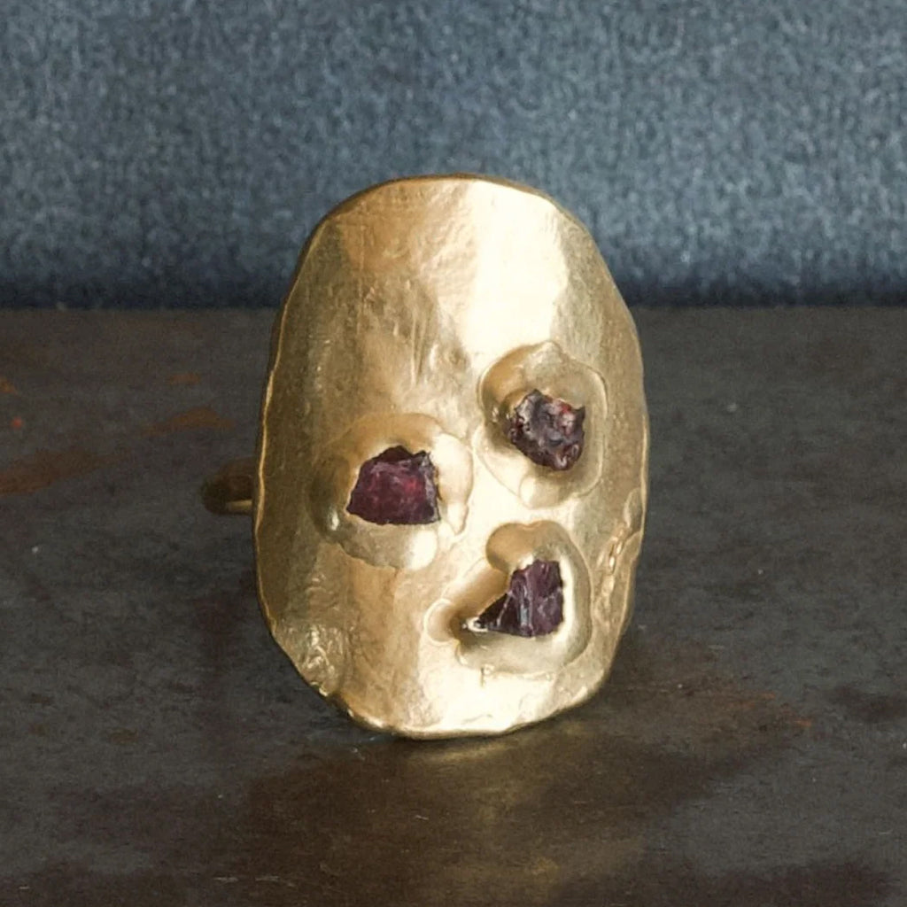 Gold ring with embedded red stones on a dark surface