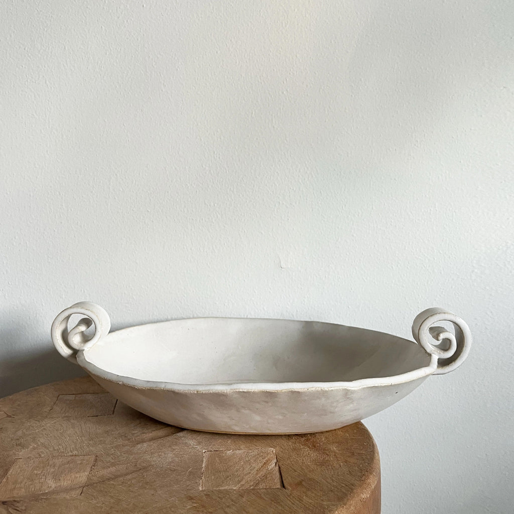 White ceramic bowl with handles on a wooden surface against a light gray background