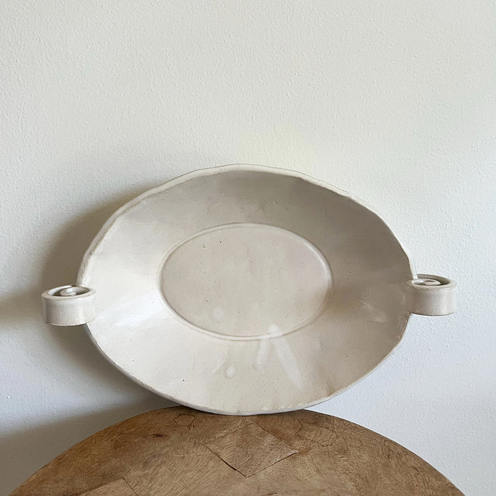 White ceramic dish with handles on a wooden surface against a light background