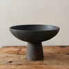 Black ceramic pedestal bowl on a wooden surface with a neutral background