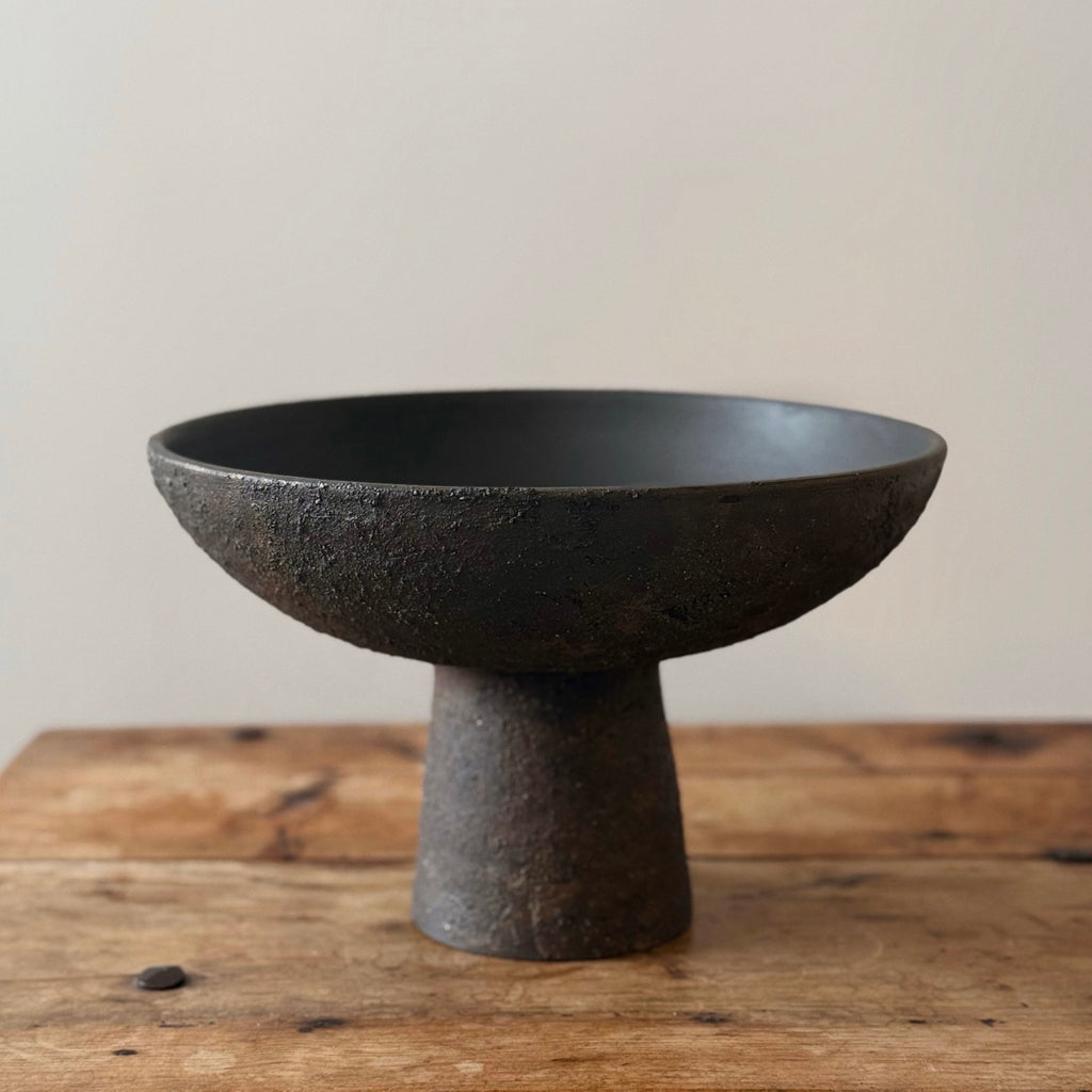 Black ceramic pedestal bowl on a wooden surface with a neutral background