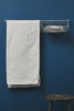 White textured towel hanging on a rack against a blue wall with a wooden stool in the foreground.