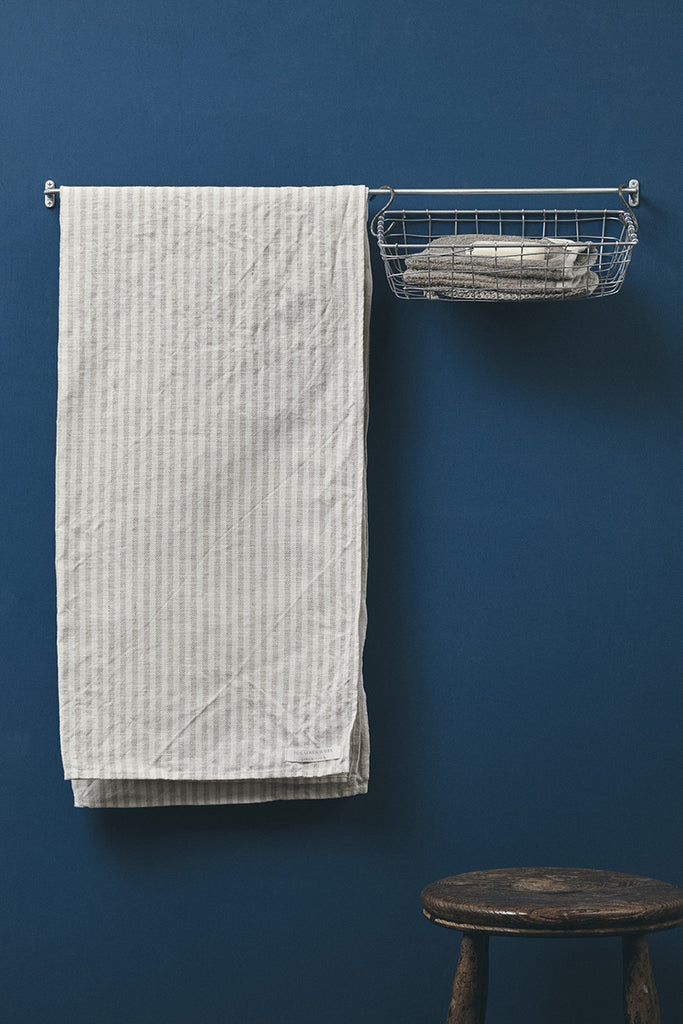 White textured towel hanging on a rack against a blue wall with a wooden stool in the foreground.